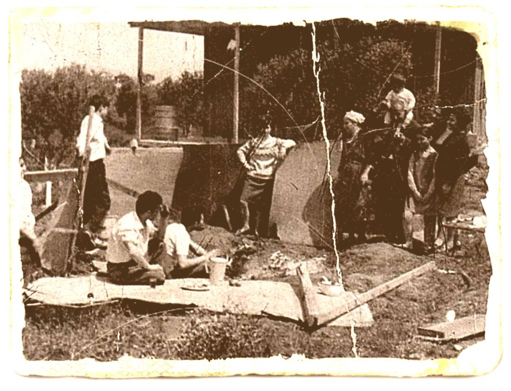 Old black-and-white photograph of a vintage outdoor family or community gathering with people enjoying a meal, nature, and social interaction.